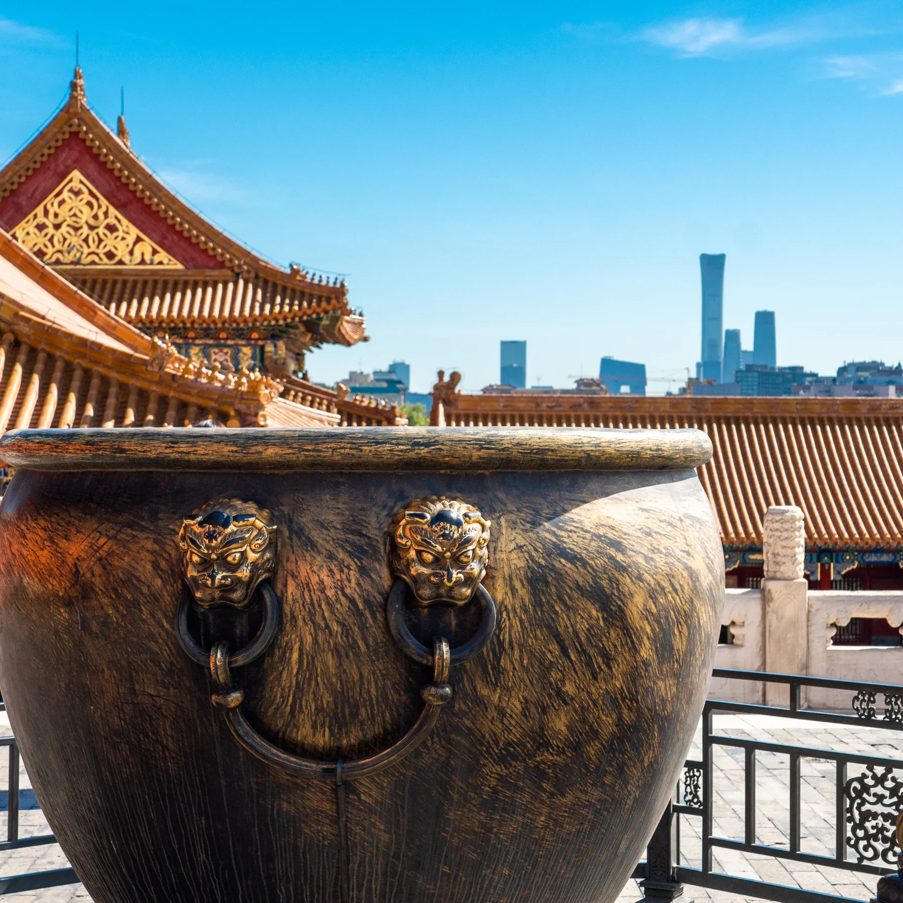 An old bronze vessel set against Beijing's temple roofs and modern skyline
